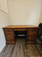 Front view of solid wood desk showing seven drawers, brass handles, and wood finish