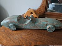 Rustic turquoise painted wood car figurine on wooden surface with a wooden massager in the background