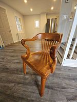 Angled front view of wooden desk chair showing curved armrest and contoured seat