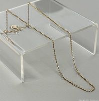 Chain draped over clear acrylic riser showing link style and clasp detail