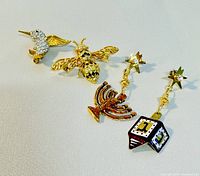 View of two gold-tone and enamel Hanukkah-themed dangle pins featuring a menorah and dreidel with star tops and rhinestone accents.