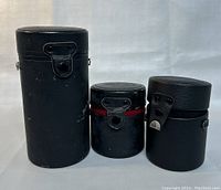 Three lens cases, varying sizes with leather or similar construction, showing minor wear.