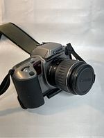 Side angled view of Canon EOS 10S camera with attached zoom lens, show grip and strap attachment