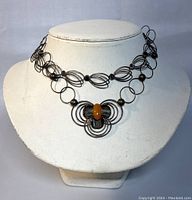 Necklace displayed on white mannequin bust showing full front view of circular wire design and amber accent pendant.