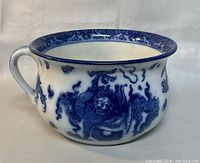 Front angle showing the blue dragon and cloud motif on the white porcelain body of the chamber pot with handle visible.