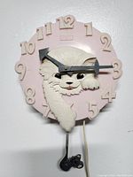 Front view of vintage 1960s pink Spartus cat wall clock showing raised white cat figure and black arrow hands.