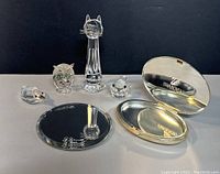 All items arranged showing cat, owl, duck, small bird figurines along with compact mirror discs and casing, on reflective surface with dark background.