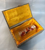 Snuff bottle displayed inside original fabric-covered box with yellow satin interior.