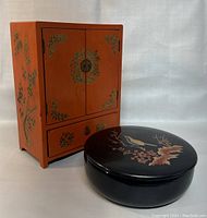 Full view of the Chinese lacquered jewelry armoire and the round black Japanese lacquer covered box placed in front of the armoire.