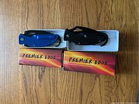 Top view showing two Premier Edge boxed survival knives in blue and black with carabiners