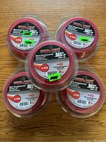 Top view of five unopened rolls of Copperhead red commercial .065 inch diameter grass trimmer line arranged in a circle on a wooden surface.