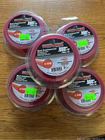 Five unopened rolls of Copperhead Red Commercial .080 inch x 50 feet grass/weed trimmer line, stacked on wooden surface.