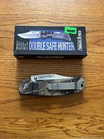 Cold Steel Double Safe Hunter folding knife closed with camouflage handle along with its box on wooden surface.