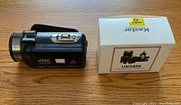 4K Ultra HD handheld video camera with two new batteries in box and charger on wooden surface.