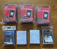 Seven card protectors in packaging and loose, showing combination of hard card holders and soft card sleeves on wooden surface.