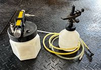 Full view of Mityvac vacuum brake bleeder showing main fluid reservoir with black lid connected to vacuum pump and yellow hoses. Smaller white plastic bottle with spray nozzle and mounting clamp included.
