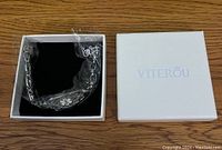 Medical ID bracelet in a white Viterou box, protective plastic partially covering the bracelet showing linked chain and ID plate.