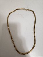 Gold plated snake necklace laid flat for full length view on light background.