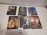 Six action DVDs arranged in two rows on flat surface. Titles visible: The 13th Warrior, Ator The Fighting Eagle, Lord Protector, Troy, The Lion in Winter.