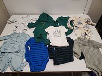 Photo showing 9 baby outfits laid out on a white surface, featuring various colors and patterns, all suitable for newborn to 6 months.
