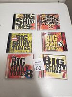 Seven Big Shiny Tunes CDs from volumes 2,3,5,7,8 stacked on a white surface with MaxSold lot tag visible.