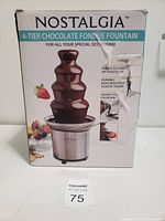 Box showing Nostalgia branding and 4-tier chocolate fountain image. Descriptions include holds 32 oz of chocolate, durable heat-resistant plastic tower, auger-style fountain.