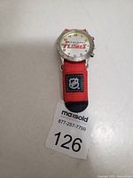 Front view of Calgary Flames wristwatch showing dial with team logo and red fabric strap with NHL logo patch.