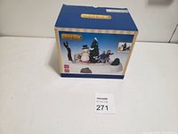 Box of Lemax Christmas holiday figurine depicting a winter scene with snowman and carolers.