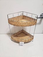 Two-tier corner shelf with woven wicker baskets and metal frame shown against white background.
