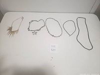Five pieces of costume jewelry displayed on a white surface including necklaces and bracelets in different styles and sizes.