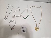 Photo of five necklaces and one bracelet arranged on a white surface with auction lot number card