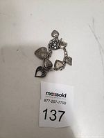 Silver-tone bracelet with six heart-shaped charms laying flat on a white surface with a lot number card next to it.
