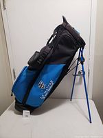 Side profile of blue and black golf bag showing stand legs and external pockets.