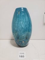 Front view of a blue hand crafted glass vase with a smooth oval shape and color flecks.