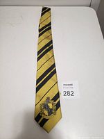 Yellow silk tie with black diagonal stripes and Hufflepuff house crest embroidered near the bottom of the tie.