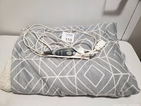 Folded gray electric blanket with white geometric patterns laid flat with attached wired controller visible.