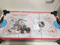 Top view of kids air hockey table showing NHL style rink surface, plastic puck, strikers with cords and accessories.