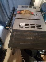 Top down view of the skill saw table showing the circular saw blade and metal vented tabletop surface with an attached black extension platform.