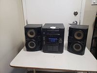 Sony stereo system including central unit and two speakers placed on a white table against a white wall