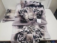 Folded queen size sheet set with clear white tiger face design in monochrome and purple tones on top of a white table.