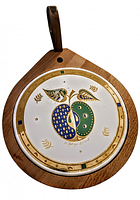 Front view of the trivet showing the round ceramic inset with blue and green apple design with gold accents on wooden base with handle.