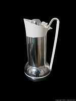 Side view of the Studio Nova thermos showing chrome body, white handle, and spout.