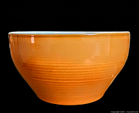 Side view of vintage orange Emile Henry ceramic mixing bowl showing ribbed texture and glossy glaze.