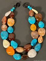 Full view of the multicolored stone necklace laid out flat, showing the arrangement of large polished beads in various natural colors and patterns.