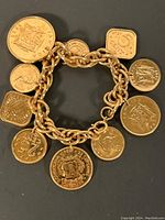 Full view of gold tone charm bracelet with eleven different coin charms in round and square shapes attached