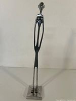 Full frontal view of the metal sculpture showing the elongated human figure on a rectangular base.