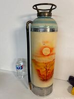 Full view of the vintage fire extinguisher with visible hand painted sunset landscape and attached hose