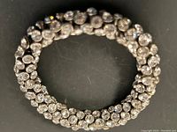 Full view of coiled multi-strand rhinestone bracelet on black background showing overall design and condition.