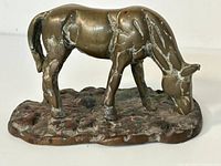 Side view of a brass horse figurine showing its texture, patina, and wear on the surface and base