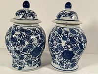 Pair of blue and white ceramic ginger jars with lids against a white background. Both jars are shown side by side with their intricate floral and vine designs clearly visible.
